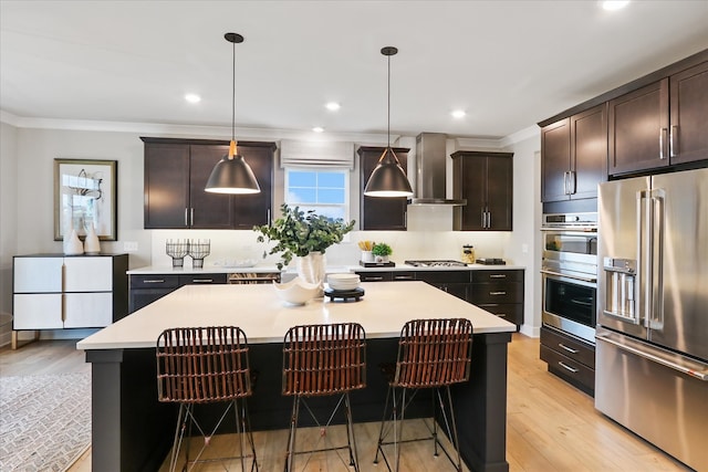 kitchen featuring a center island, stainless steel appliances, wall chimney range hood, crown molding, and pendant lighting