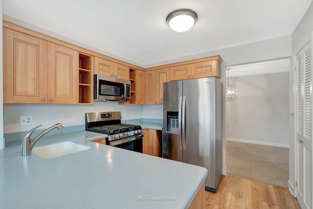 kitchen featuring light wood finished floors, stainless steel appliances, light countertops, open shelves, and a sink