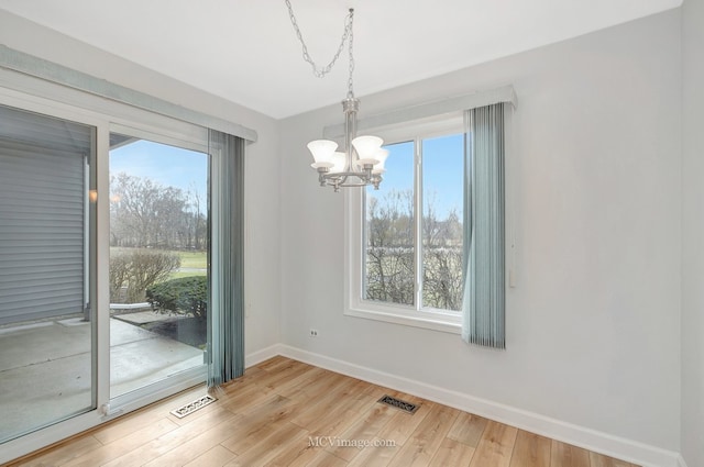 unfurnished dining area with visible vents, a notable chandelier, baseboards, and wood finished floors