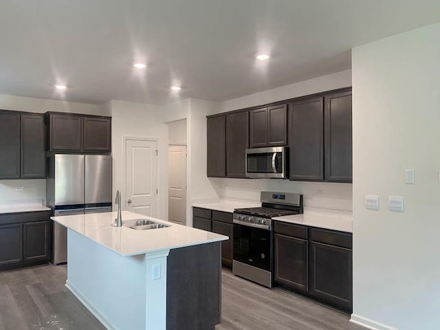 kitchen featuring appliances with stainless steel finishes, dark brown cabinetry, sink, a center island with sink, and light hardwood / wood-style flooring