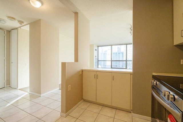 kitchen featuring light tile patterned flooring, cream cabinets, and stainless steel range oven