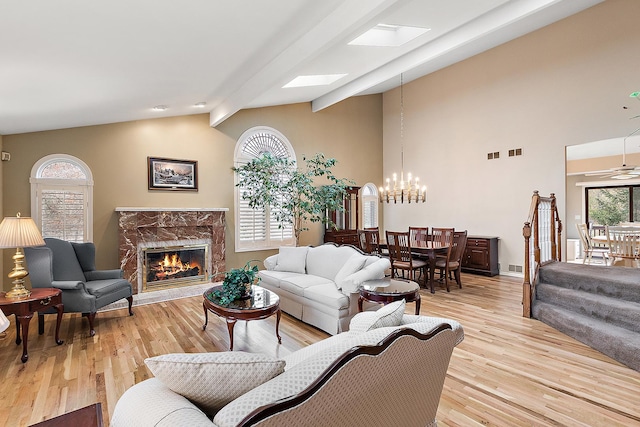 living room featuring lofted ceiling with beams, light hardwood / wood-style floors, a premium fireplace, and ceiling fan with notable chandelier