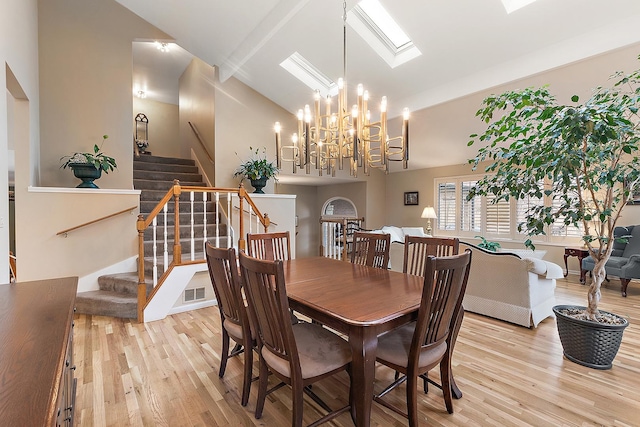 dining area featuring an inviting chandelier, light wood-type flooring, high vaulted ceiling, and a skylight