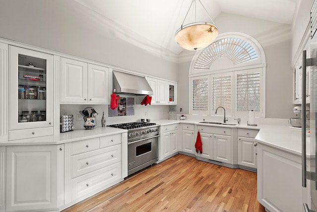 kitchen featuring lofted ceiling, wall chimney range hood, sink, high end stainless steel range oven, and white cabinetry