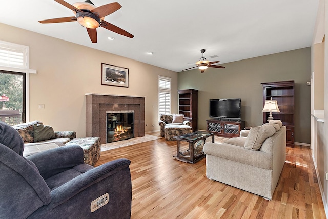 living room featuring light hardwood / wood-style floors, ceiling fan, and a tiled fireplace