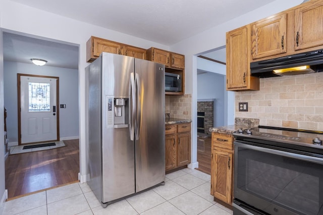 kitchen with stainless steel appliances, stone counters, light tile patterned floors, and decorative backsplash