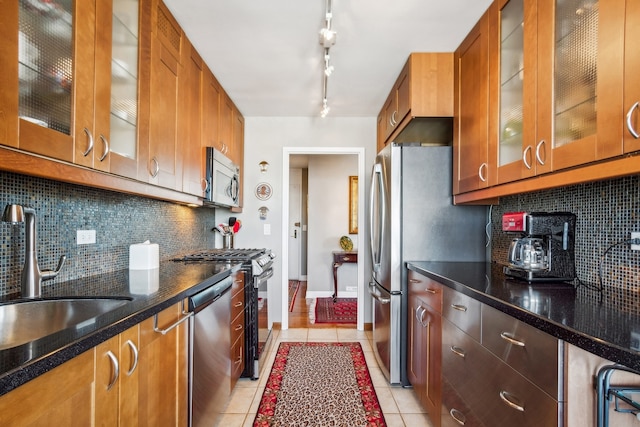 kitchen with appliances with stainless steel finishes, backsplash, light tile patterned floors, and dark stone counters