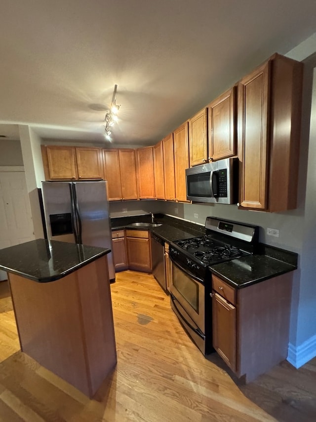 kitchen with rail lighting, sink, dark stone countertops, light wood-type flooring, and appliances with stainless steel finishes