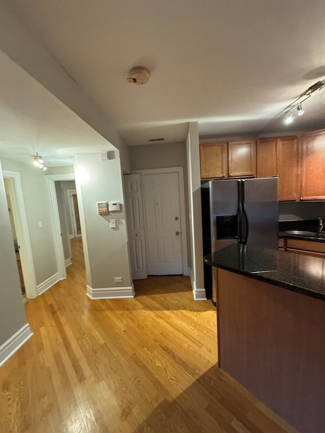 kitchen with stainless steel fridge with ice dispenser, dark stone counters, and light hardwood / wood-style flooring