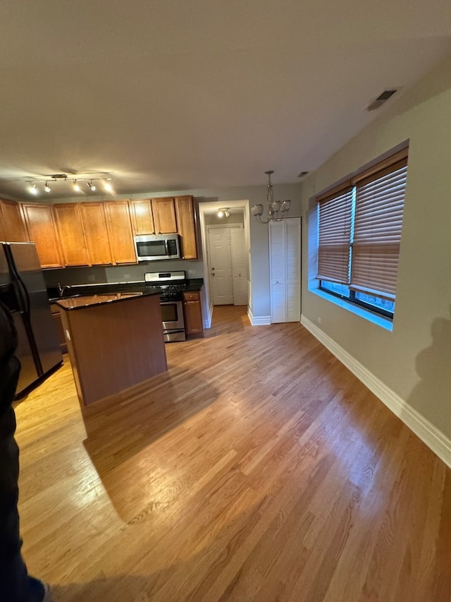 kitchen with pendant lighting, light wood-type flooring, appliances with stainless steel finishes, a notable chandelier, and a kitchen island