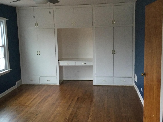 unfurnished bedroom featuring ceiling fan, built in desk, and dark wood-type flooring