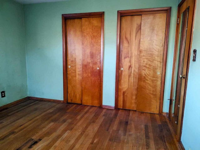 unfurnished bedroom with dark hardwood / wood-style flooring and two closets