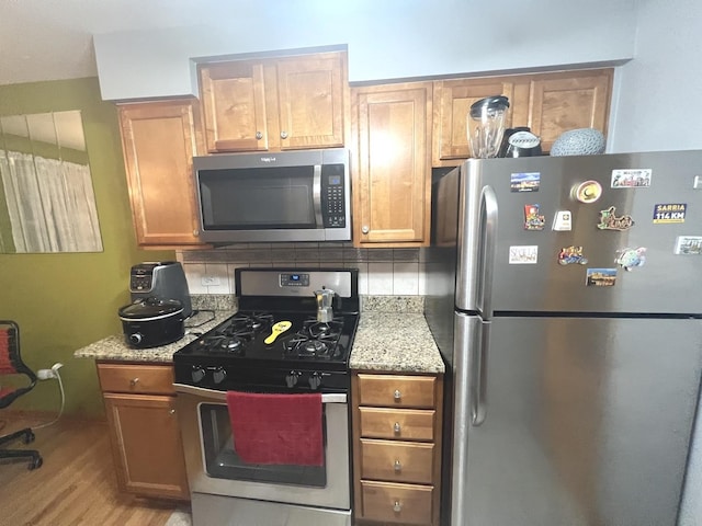 kitchen featuring decorative backsplash, light hardwood / wood-style floors, light stone counters, and stainless steel appliances