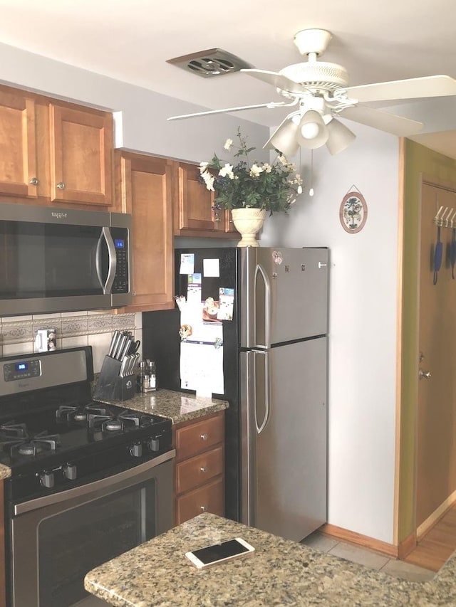 kitchen with decorative backsplash, ceiling fan, appliances with stainless steel finishes, light tile patterned flooring, and light stone counters