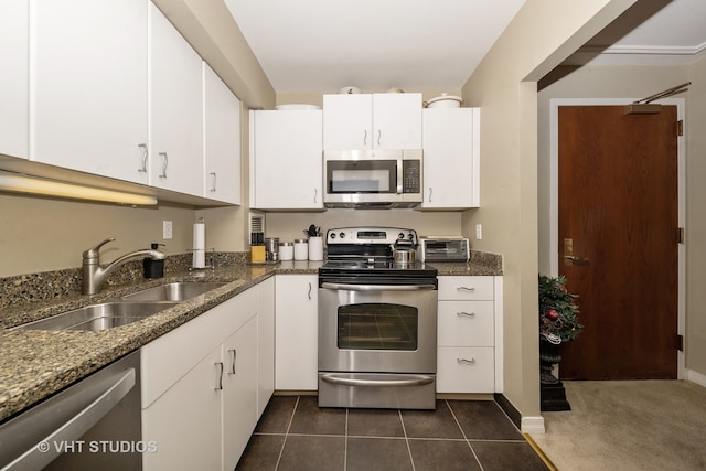 kitchen with appliances with stainless steel finishes, dark stone counters, sink, dark tile patterned flooring, and white cabinetry