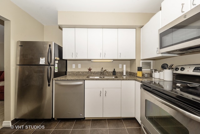 kitchen with stainless steel appliances, dark tile patterned floors, sink, dark stone countertops, and white cabinets