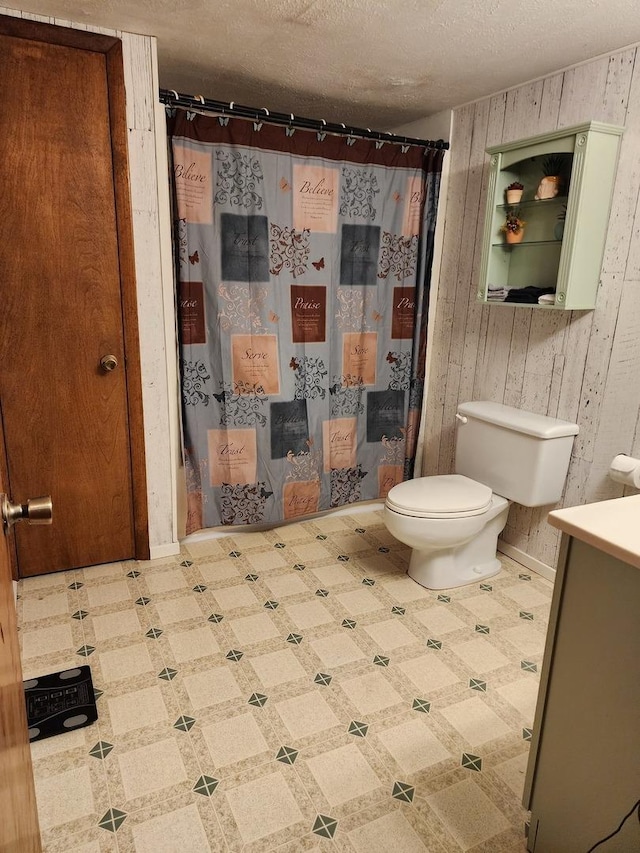 bathroom featuring wooden walls, vanity, walk in shower, toilet, and a textured ceiling