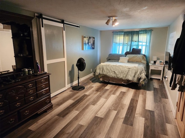 bedroom featuring wood-type flooring, a barn door, and a textured ceiling