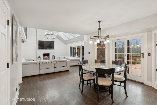 dining room featuring french doors, dark wood-type flooring, a notable chandelier, vaulted ceiling, and a fireplace