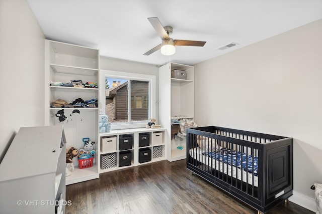 bedroom with dark hardwood / wood-style flooring, a nursery area, and ceiling fan