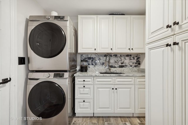 laundry room with sink, light hardwood / wood-style floors, cabinets, and stacked washer and dryer