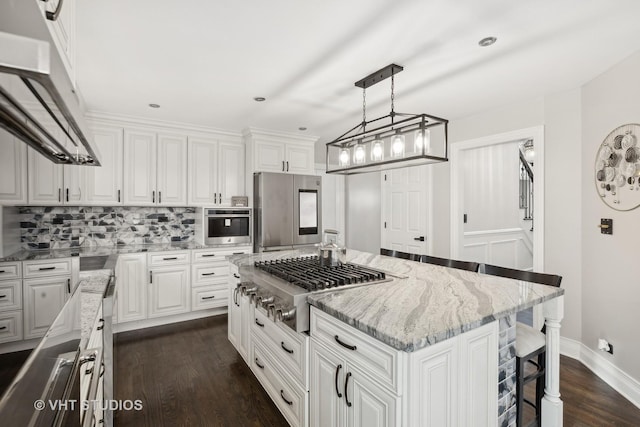 kitchen with white cabinets, appliances with stainless steel finishes, dark hardwood / wood-style flooring, and a kitchen island