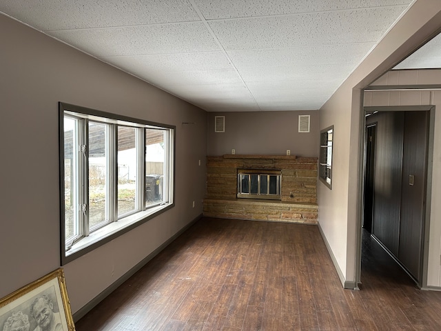 unfurnished living room with a paneled ceiling, a fireplace, and dark wood-type flooring