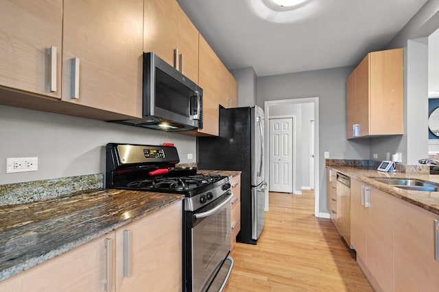 kitchen with light hardwood / wood-style floors, dark stone countertops, sink, and appliances with stainless steel finishes