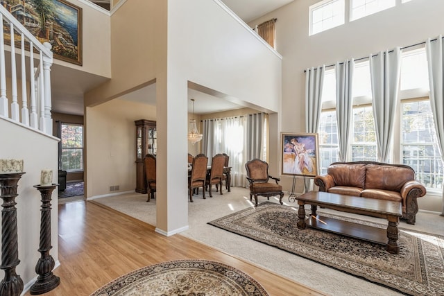 living room featuring plenty of natural light, light wood-type flooring, a towering ceiling, and an inviting chandelier