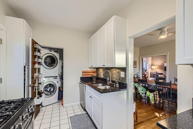 kitchen featuring stacked washer / dryer, sink, dark stone countertops, and white cabinets