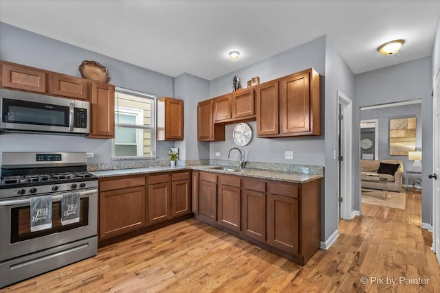 kitchen with light stone counters, sink, light wood-type flooring, and appliances with stainless steel finishes