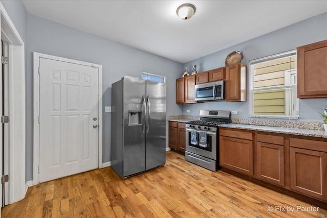 kitchen featuring appliances with stainless steel finishes, light wood-type flooring, and light stone counters