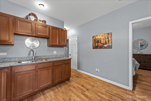 kitchen with light stone countertops, light wood-type flooring, and sink