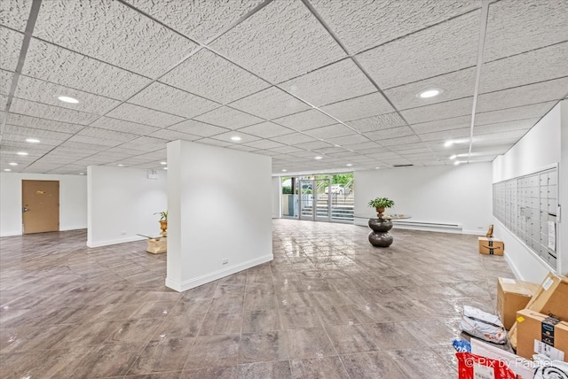 basement with a paneled ceiling, a mail area, and a baseboard heating unit