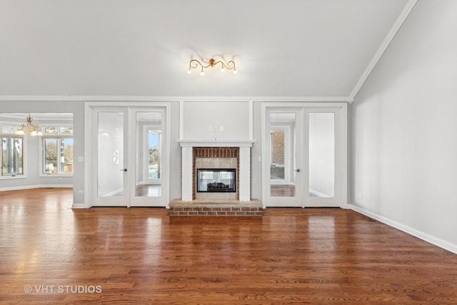 unfurnished living room featuring crown molding, dark hardwood / wood-style flooring, a chandelier, and a brick fireplace