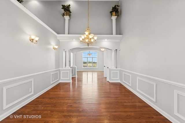 hallway with dark hardwood / wood-style floors, ornate columns, crown molding, and an inviting chandelier