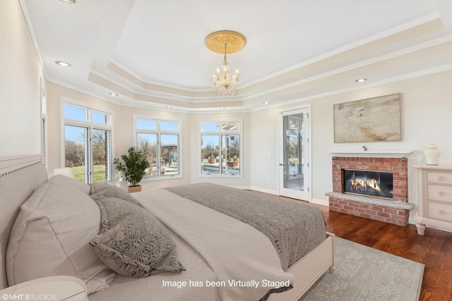 bedroom featuring dark hardwood / wood-style flooring, ornamental molding, access to outside, a raised ceiling, and a fireplace