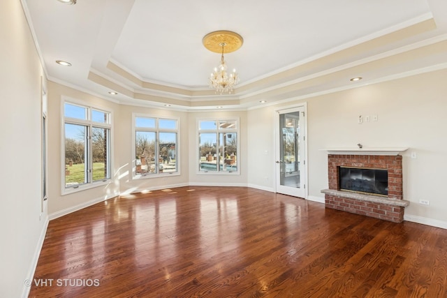 unfurnished living room with a brick fireplace, dark hardwood / wood-style floors, a notable chandelier, crown molding, and a tray ceiling