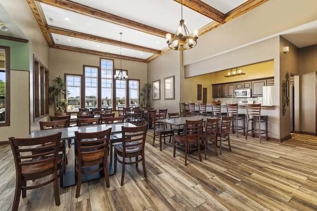 dining room with beam ceiling, wood-type flooring, a high ceiling, and an inviting chandelier