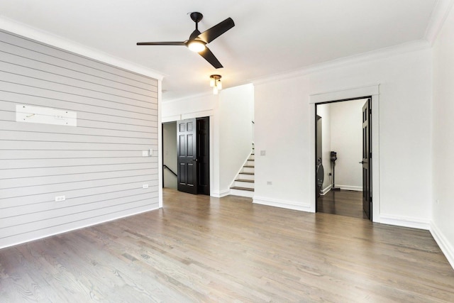 empty room featuring wood-type flooring, crown molding, ceiling fan, and wooden walls