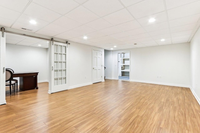 interior space featuring a barn door, a drop ceiling, and light hardwood / wood-style floors