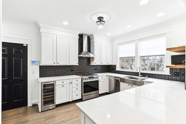 kitchen with white cabinetry, beverage cooler, wall chimney range hood, appliances with stainless steel finishes, and light wood-type flooring