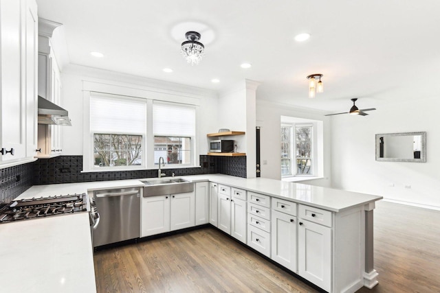 kitchen with kitchen peninsula, backsplash, stainless steel appliances, sink, and white cabinetry