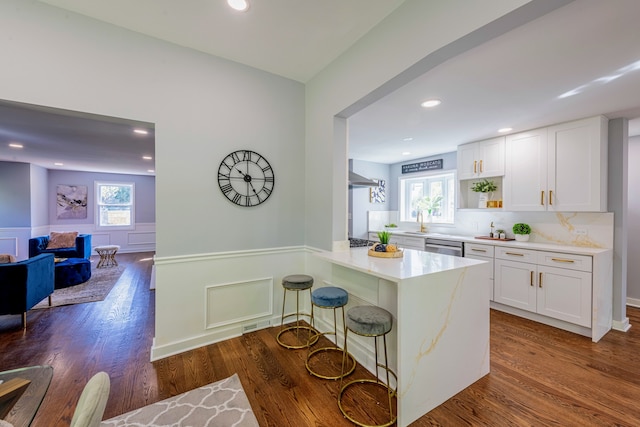 kitchen featuring kitchen peninsula, a kitchen bar, white cabinetry, and a healthy amount of sunlight