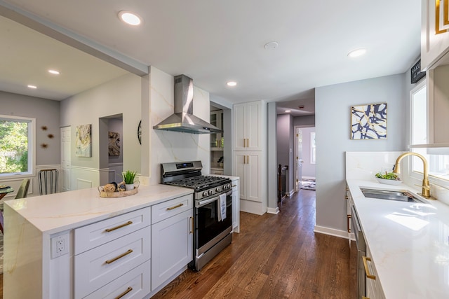 kitchen featuring stainless steel gas range oven, wall chimney exhaust hood, sink, dark hardwood / wood-style floors, and white cabinetry