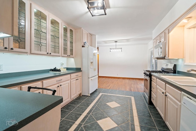 kitchen with light brown cabinetry, white appliances, sink, dark tile patterned flooring, and hanging light fixtures