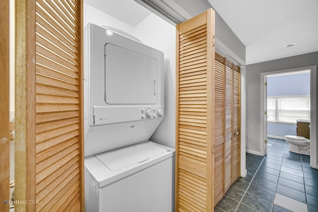 laundry room with stacked washer and dryer and dark tile patterned flooring