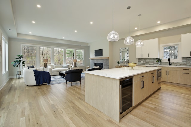 kitchen featuring light stone countertops, a kitchen island, light hardwood / wood-style floors, wine cooler, and stainless steel microwave