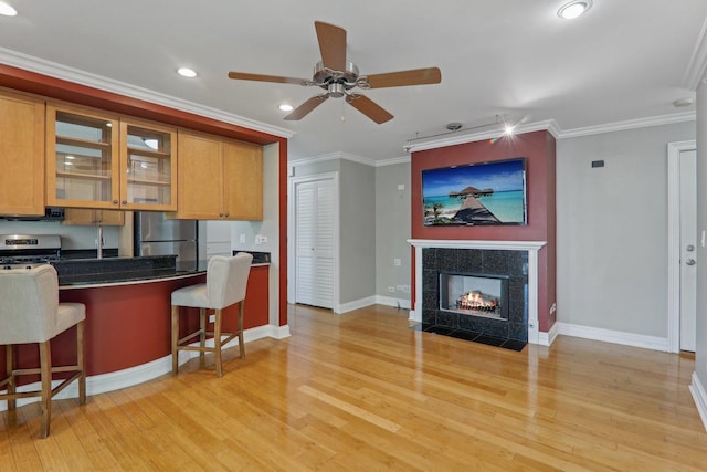 kitchen with a breakfast bar, light hardwood / wood-style flooring, ornamental molding, a high end fireplace, and stainless steel appliances