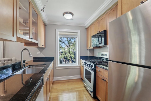 kitchen featuring sink, crown molding, dark stone counters, stainless steel appliances, and light hardwood / wood-style floors